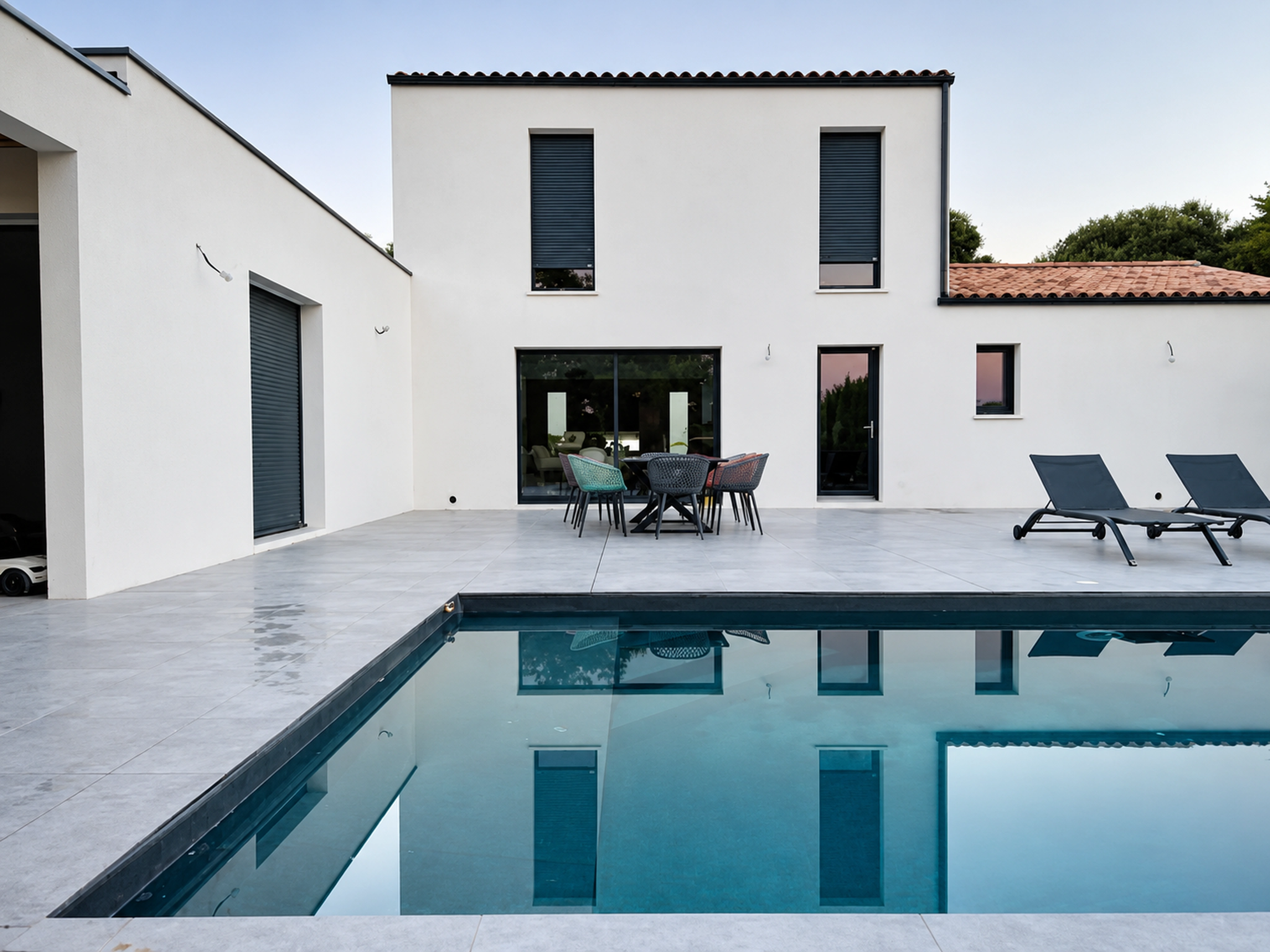 Réalisation ABK : piscine aux lignes contemporaines et terrasse devant une maison blanche